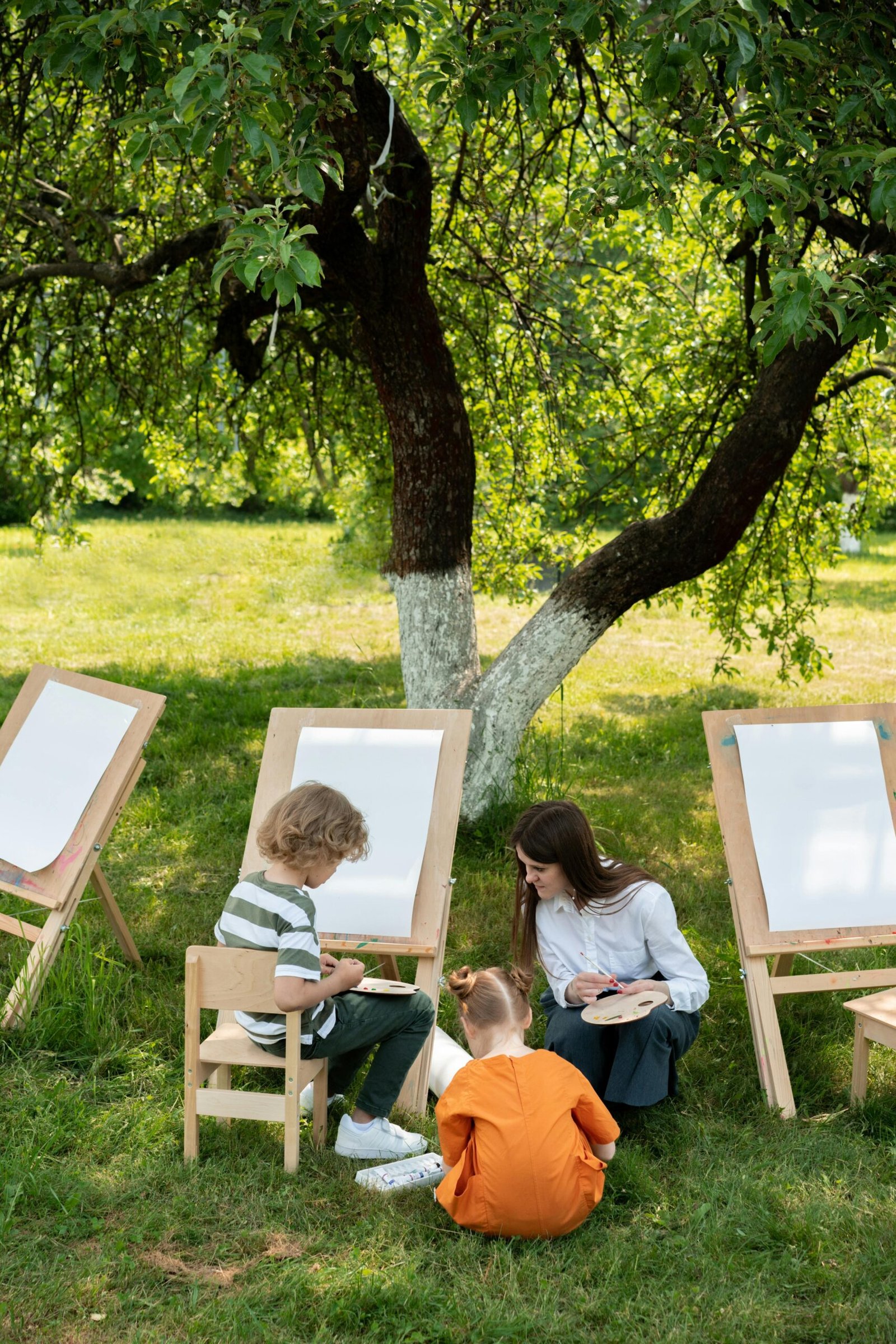 Children engaging in outdoor painting on a sunny day in a garden.